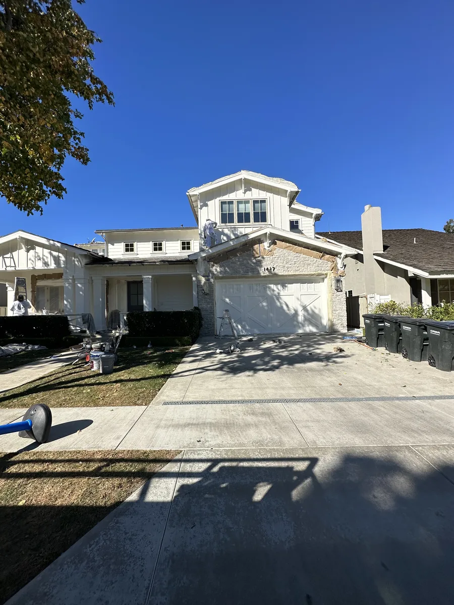 Two-story house with ladders, drop cloths and painting equipment along the driveway