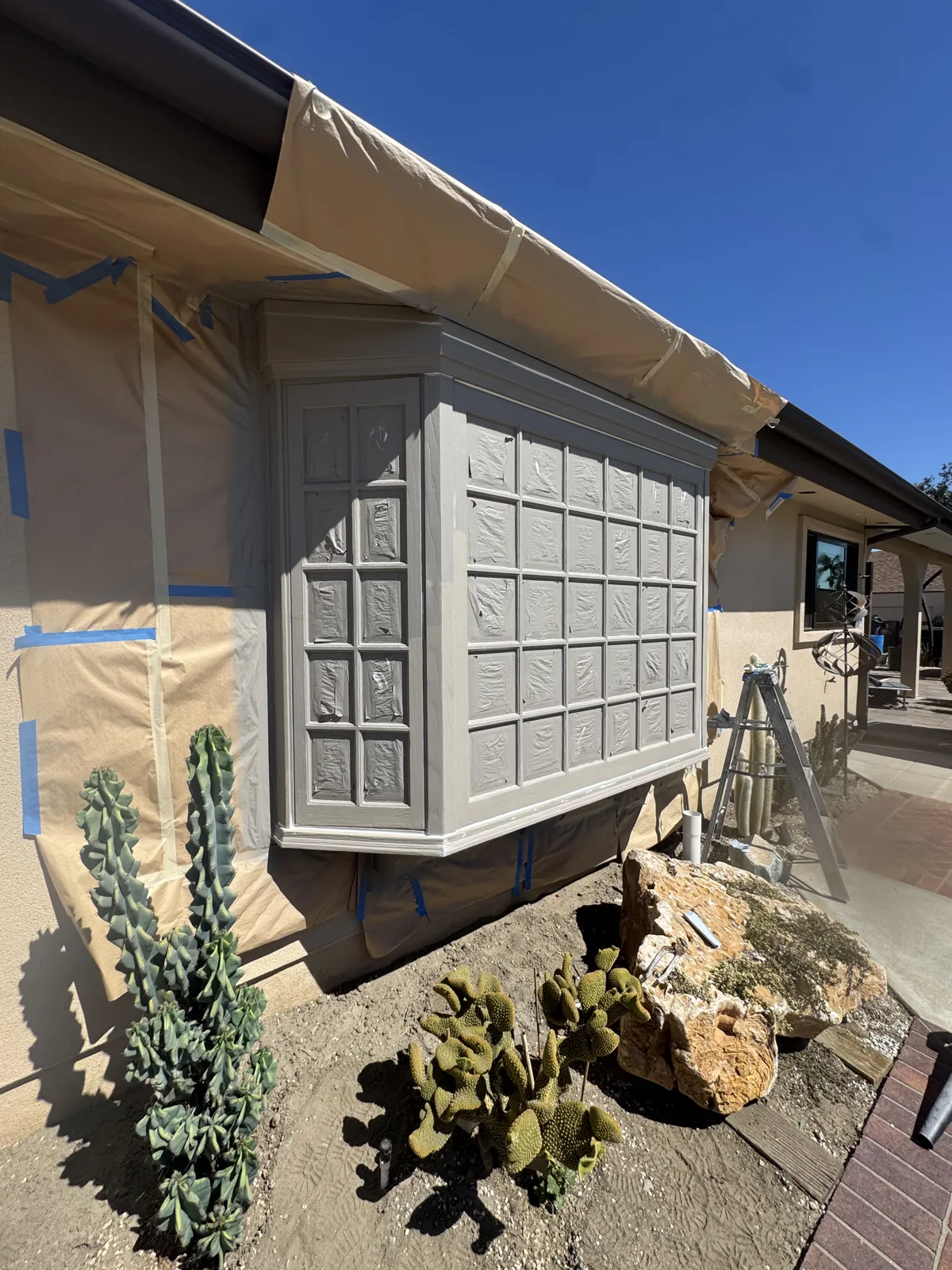 Bay window and adjacent stucco with paper masking and tape protecting surrounding surfaces