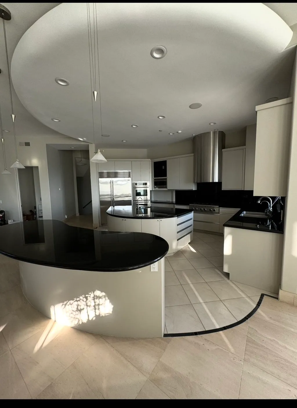 White kitchen with black countertops, curved island, and tile floor