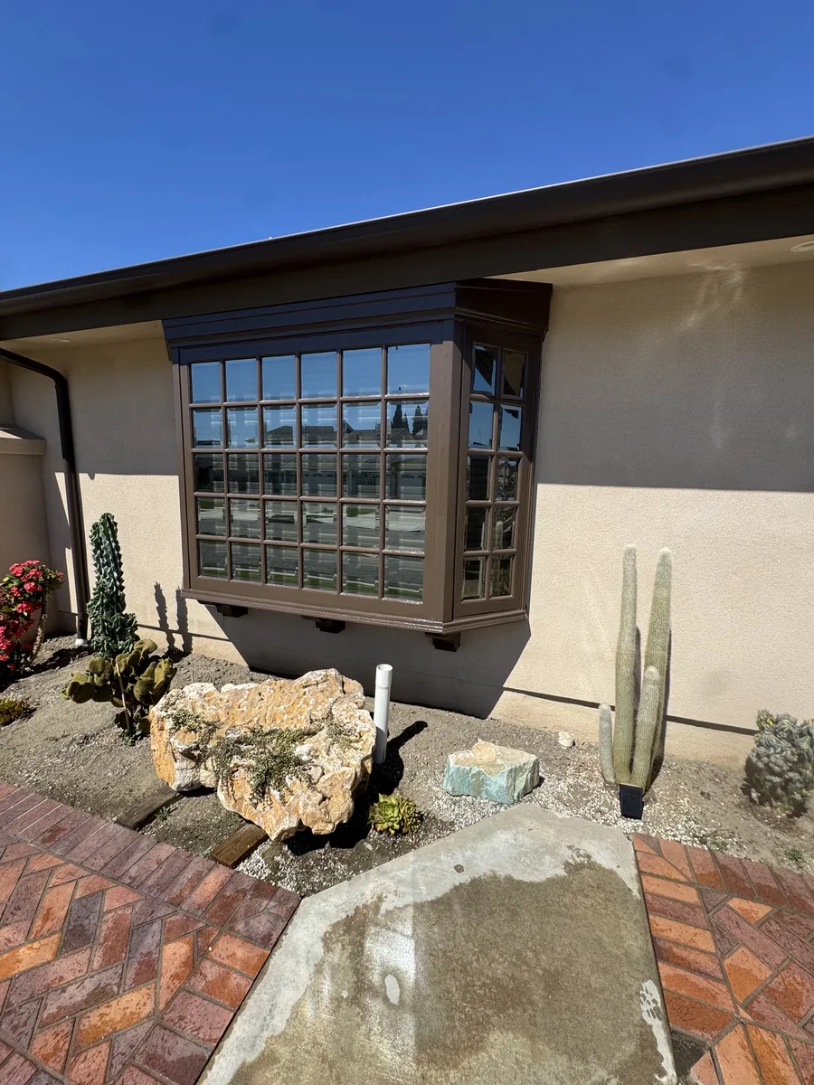 Dark-stained wood bay window trim on a stucco exterior with brick paving and desert landscaping