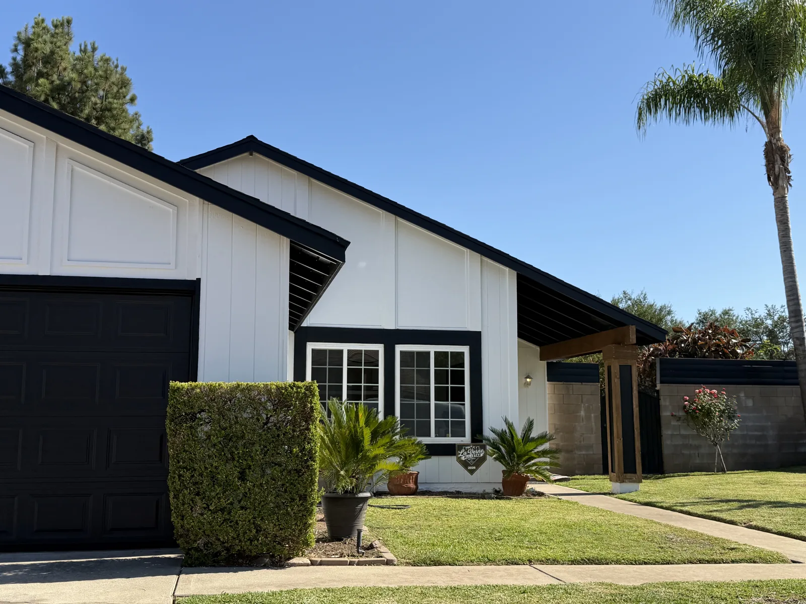 White single-story house with black fascia, window trim and garage door beside a green lawn