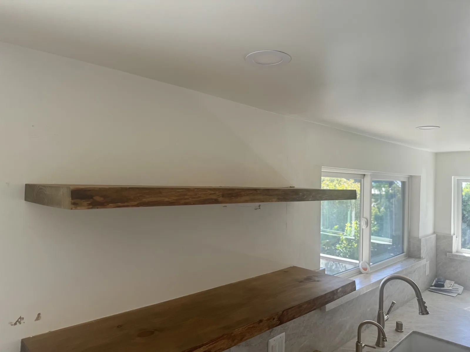 Bright kitchen with natural-wood floating shelves on a white wall above a sink