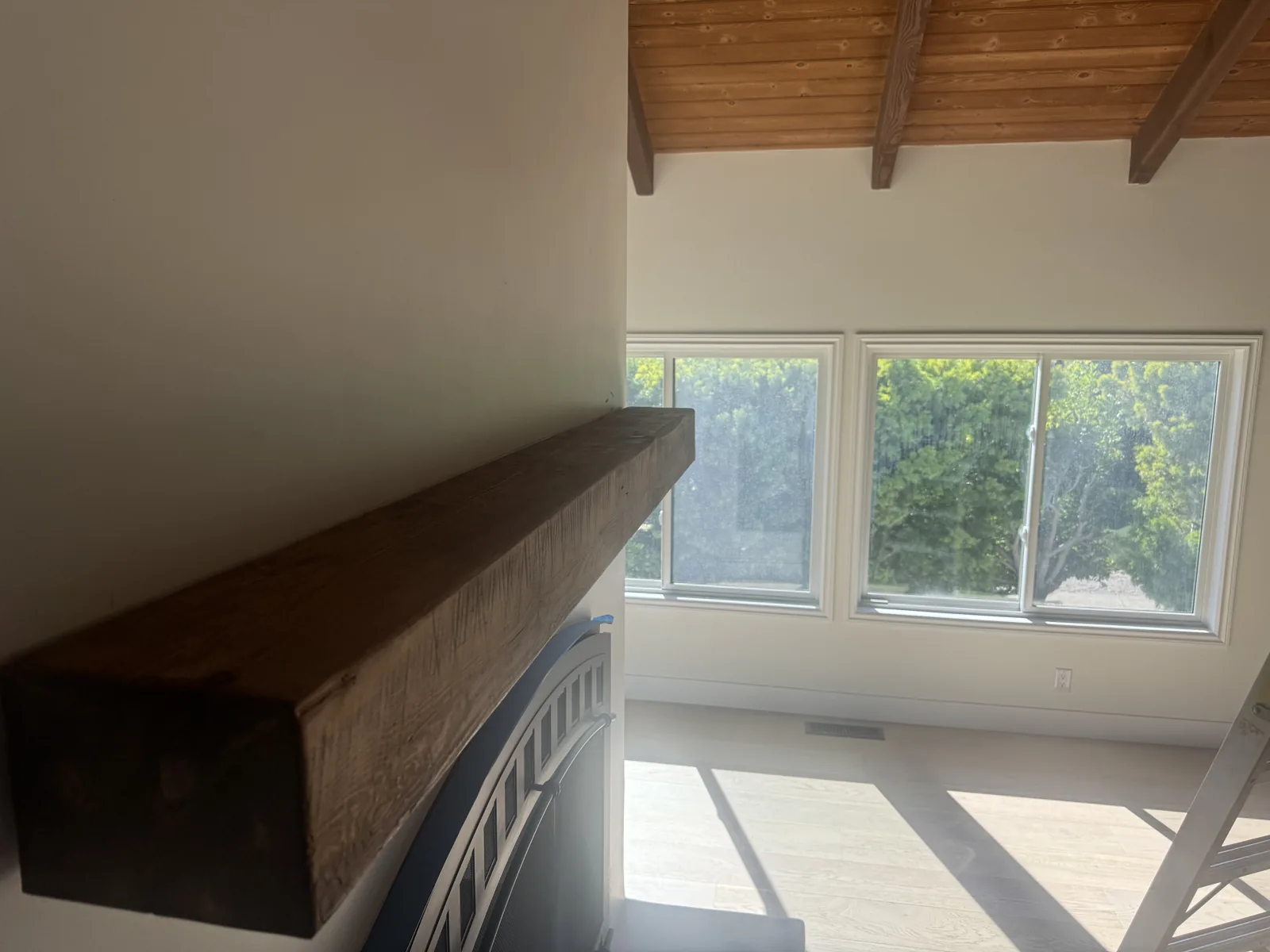 Natural wood fireplace mantel and exposed ceiling beams in a bright white room