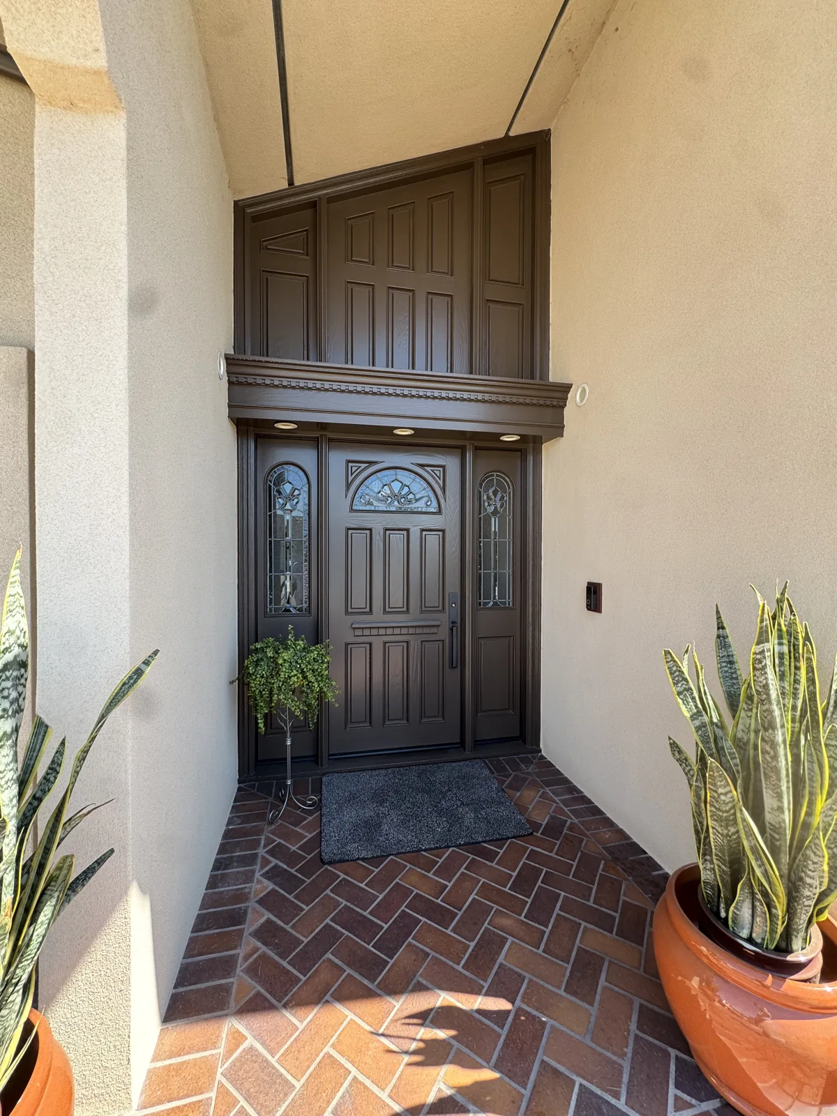 Ornate dark entry door and tall surrounding wood trim with stucco walls and a brick porch
