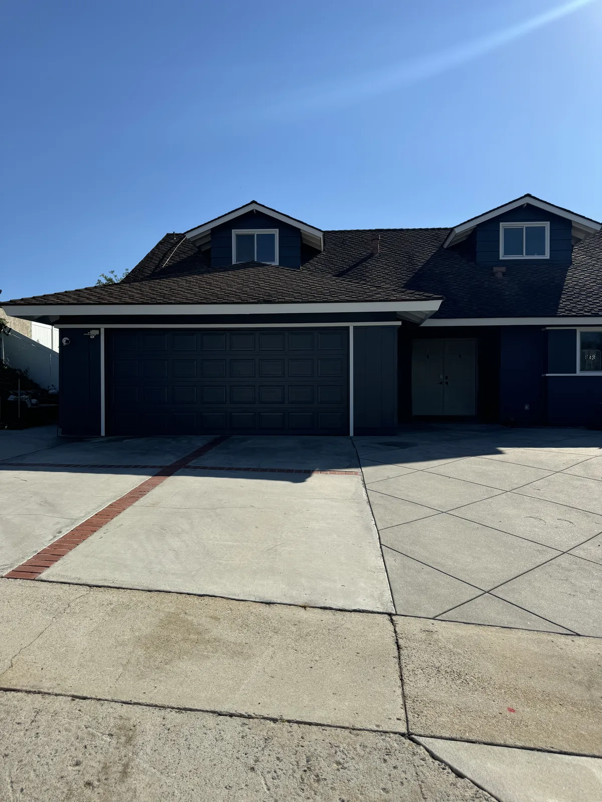 Two-story house with deep-toned walls, white trim and matching dark garage doors above a concrete driveway