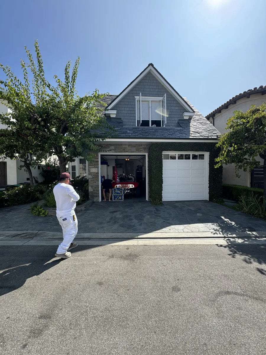 Painter in white work clothes walking up the driveway of a two-story house with an open garage